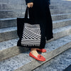 Schwarze TAKE YOUR BAG mit weißem LINEAR Design aus 100% Bio-Baumwolle, NEUTRAL® und FAIRTRADE® zertifiziert getragen von einer Frau mit roten Schuhen auf der Treppe.