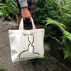 Beige TAKE YOUR BAG mit schwarzem ME & YOU Design aus 100% Bio-Baumwolle, NEUTRAL® und FAIRTRADE® zertifiziert, getragen von einem Mann im Garten.