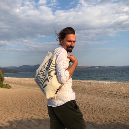 Beige TAKE YOUR BAG with black FISH design made of 100% organic cotton, NEUTRAL® and FAIRTRADE® certified on the beach.