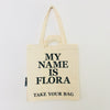 Beige TAKE YOUR BAG made of 100% organic cotton, NEUTRAL® and FAIRTRADE® certified with black MY NAME IS FLORA design.