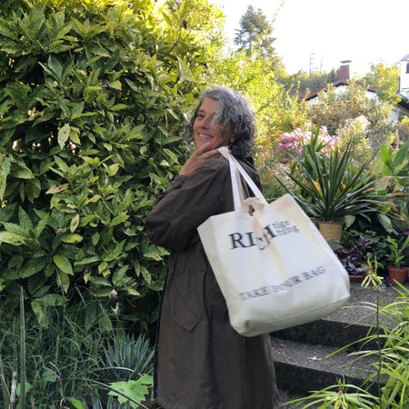 Beige TAKE YOUR BAG aus 100% Bio-Baumwolle, NEUTRAL® und FAIRTRADE® zertifiziert mit schwarzem RICHTIGE RICHTUNG Design, getragen von einer Frau im Garten.