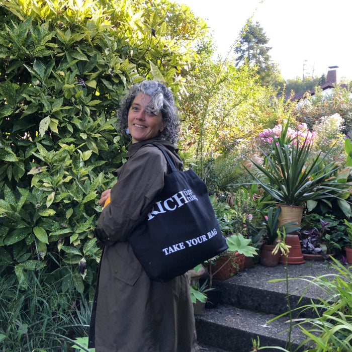 Schwarze TAKE YOUR BAG mit weißem RICHTIGE RICHTUNG Design aus 100% Bio-Baumwolle, NEUTRAL® und FAIRTRADE® zertifiziert. getragen von einer Frau im Garten.