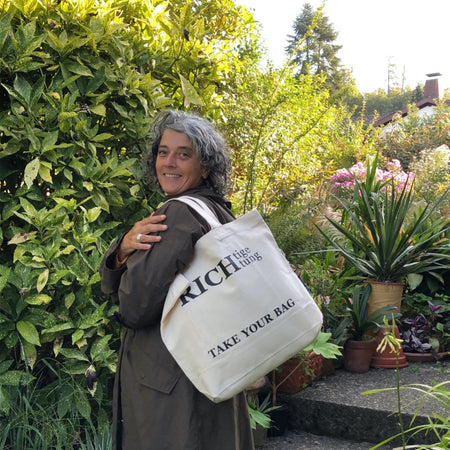 Beige TAKE YOUR BAG mit schwarzem RICHTIGE RICHTUNG Design aus 100% Bio-Baumwolle, NEUTRAL® und FAIRTRADE® zertifiziert, getragen von einer Frau im Garten.