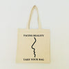 A beige cotton tote bag with a black design that reads 'FACING REALITY. TAKE YOUR BAG.'