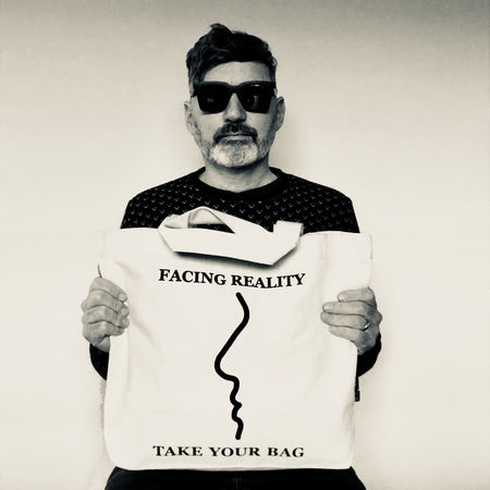 Beige TAKE YOUR BAG mit schwarzem FACING REALITY Design aus 100% Bio-Baumwolle, NEUTRAL® und FAIRTRADE® zertifiziert, getragen von einem Mann mit der schwarzen Sonnenbrille.