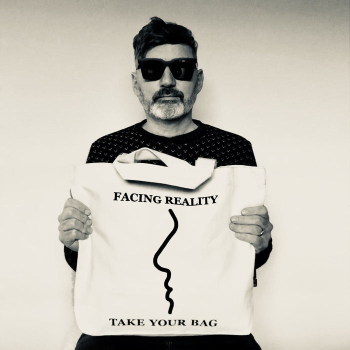 Beige TAKE YOUR BAG mit schwarzem FACING REALITY Design aus 100% Bio-Baumwolle, NEUTRAL® und FAIRTRADE® zertifiziert, getragen von einem Mann mit der schwarzen Sonnenbrille.