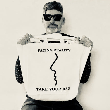 Beige TAKE YOUR BAG made of 100% organic cotton, NEUTRAL® and FAIRTRADE® certified with black FACING REALITY design getragen von einem Mann mit schwarzer Sonnenbrille.
