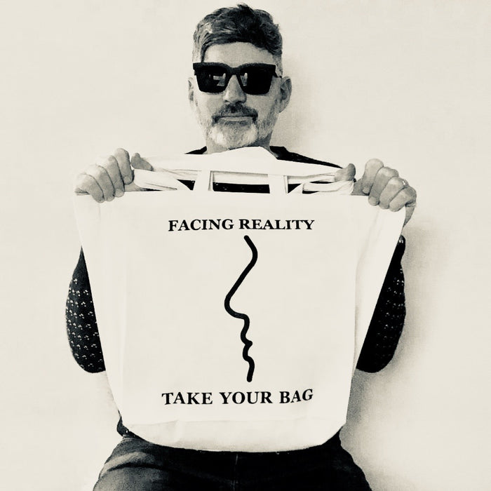 Beige TAKE YOUR BAG made of 100% organic cotton, NEUTRAL® and FAIRTRADE® certified with black FACING REALITY design getragen von einem Mann mit schwarzer Sonnenbrille.