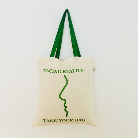 A beige canvas tote bag with a green text graphic design that reads 'FACING REALITY take your bag'.