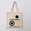 A beige cotton tote bag with a black 'UNIVERSal' logo and the text 'TAKE YOUR BAG' printed on the front.