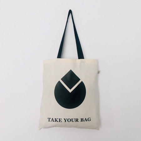 A beige cotton bag with a black handle featuring a black geometric water drop design and the text 'TAKE YOUR BAG' on the front.