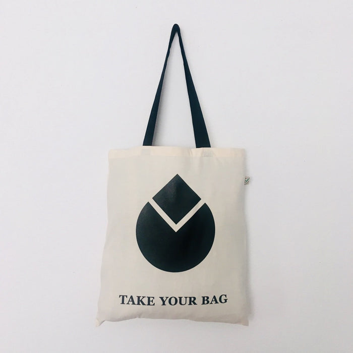 A beige cotton bag with a black handle featuring a black geometric water drop design and the text 'TAKE YOUR BAG' on the front.